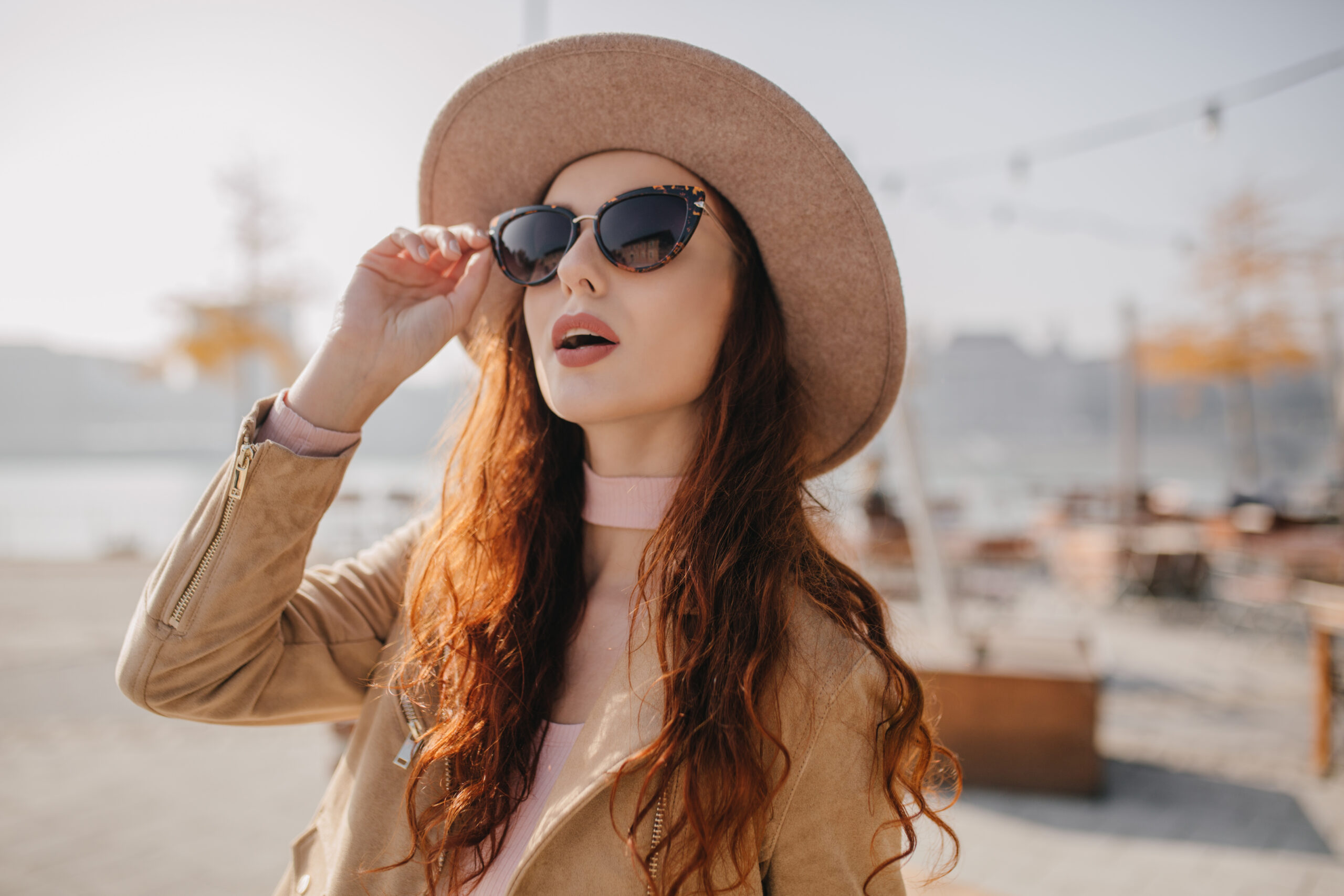 curious ginger girl touching her sunglasses. outdoor portrait of interested red haired woman looking up with mouth open..